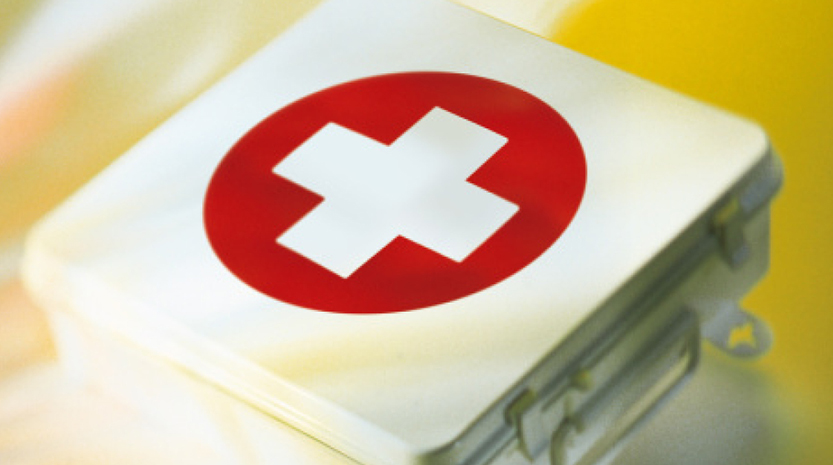 A metal first aid kit with a large red plus sign on top. The box sits atop something yellow.