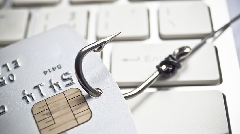 A shiny fish hook strung through a plastic credit card sits atop a computer keyboard.