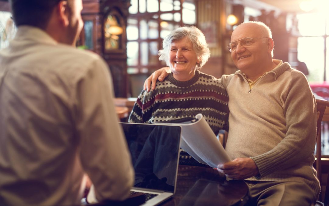 An elderly couple sits smiling across a table in a law office from a business man with a laptop.